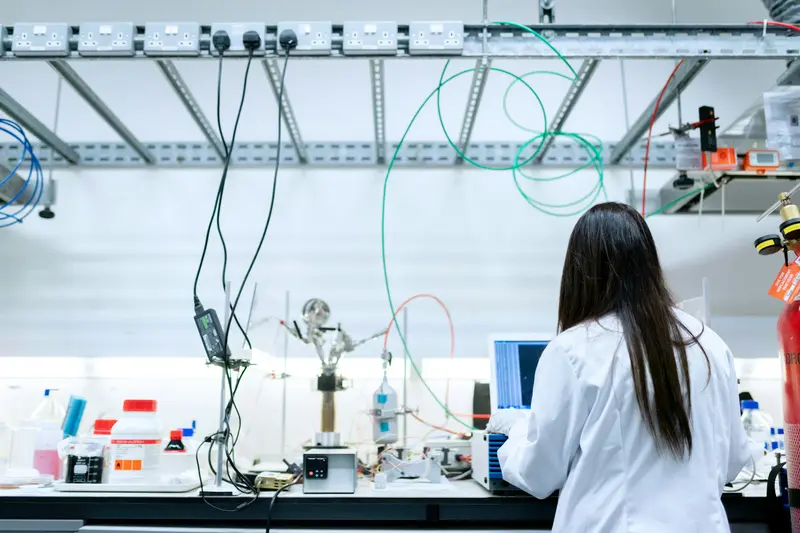 Researcher in a lab coat working at a laptop beside instrument benches